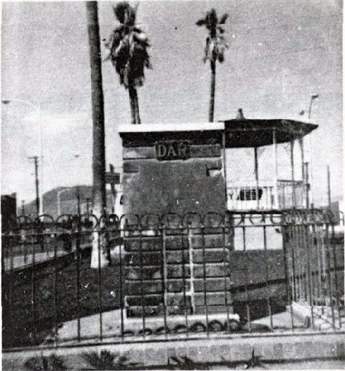 A vintage snapshot of a brick marker base with “DAR” at the top and a decorative iron fence on at least two sides in a parklike setting. An original Spanish Presidio gateway.